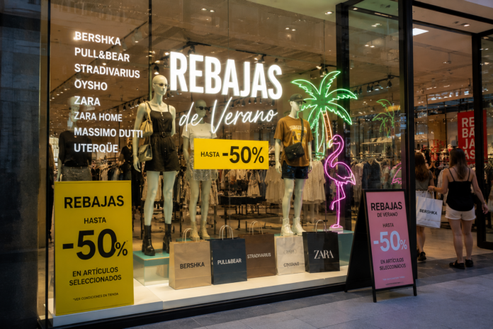 Escaparate moderno de moda con letreros de rebajas de verano, bolsas de compras, prendas de Bershka, Pull&Bear y otras marcas de Inditex exhibidas en vitrinas contemporáneas, ambiente urbano y comercial, estilo realista, iluminación vibrante, ultra detallado, formato periodístico.